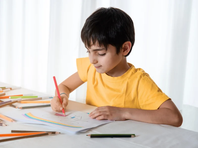 Garçon concentré coloriant un dessin d'arc-en-ciel aux crayons