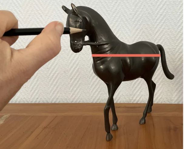 Main et crayon mesurant les proportions d'une sculpture de cheval